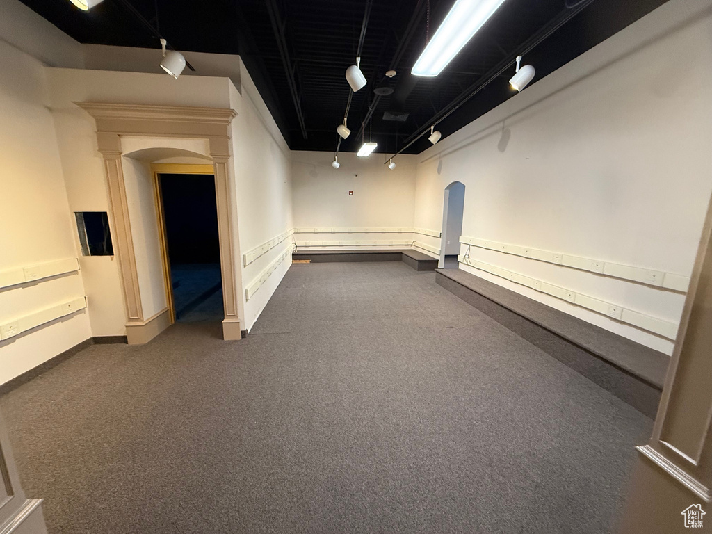 Finished below grade area featuring arched walkways, baseboards, dark colored carpet, and track lighting
