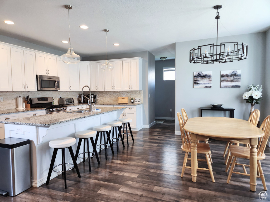 Kitchen featuring white cabinetry, a kitchen breakfast bar, dark wood-type flooring, appliances with stainless steel finishes, and a center island with sink