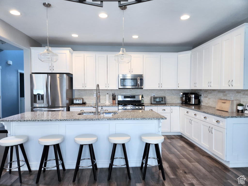 Kitchen featuring sink, stainless steel appliances, white cabinets, and hanging light fixtures