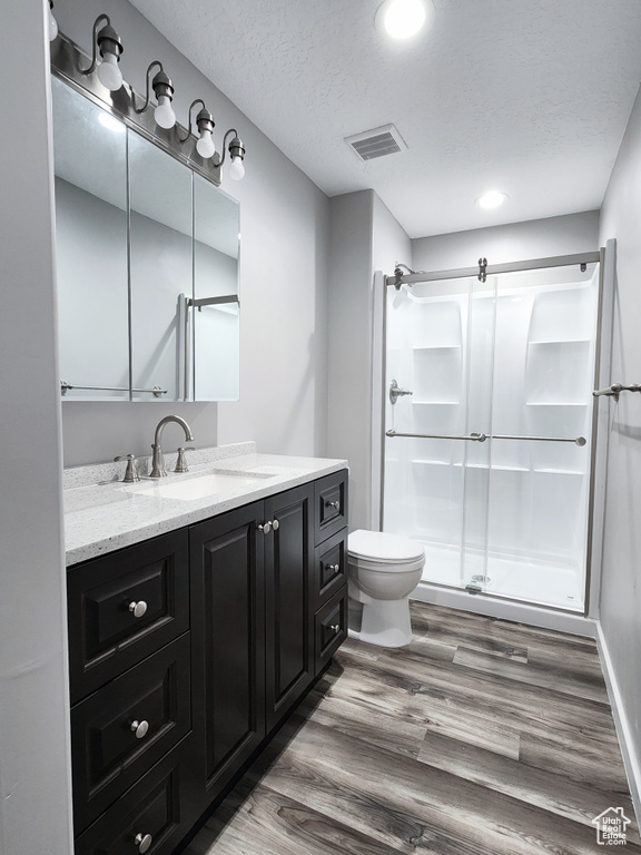 Bathroom with a textured ceiling, vanity, an enclosed shower, hardwood / wood-style floors, and toilet