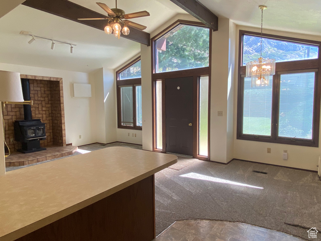 Foyer with ceiling fan with notable chandelier, rail lighting, a wood stove, carpet, and vaulted ceiling