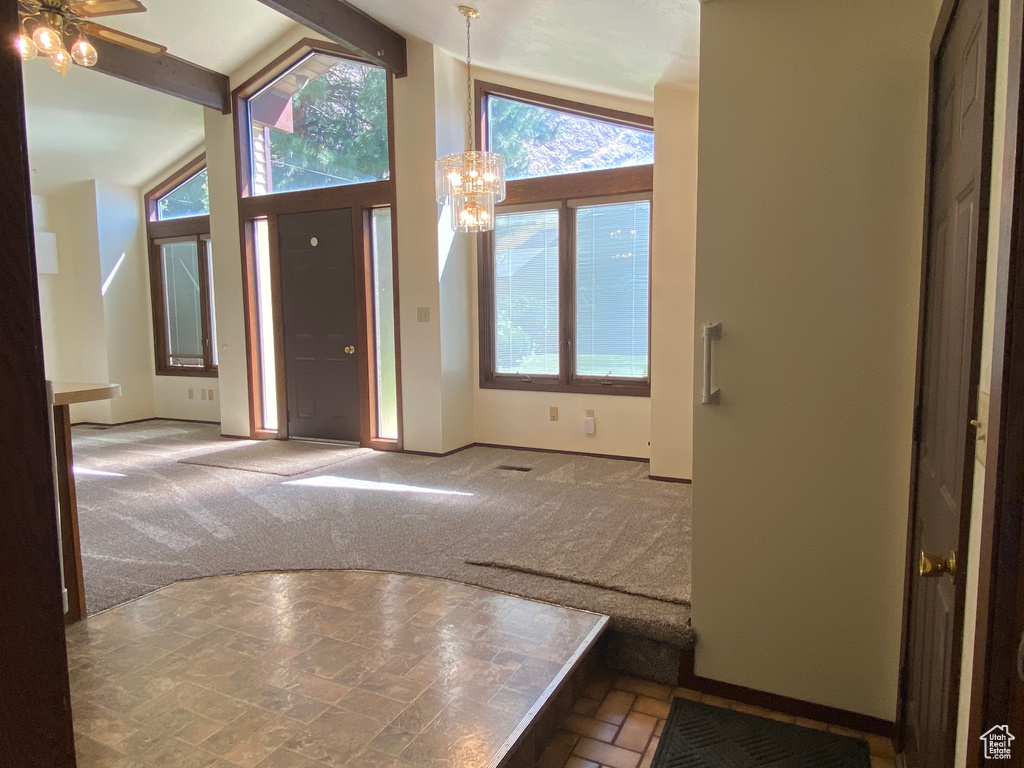 Carpeted foyer entrance with ceiling fan with notable chandelier, lofted ceiling with beams, and a wealth of natural light