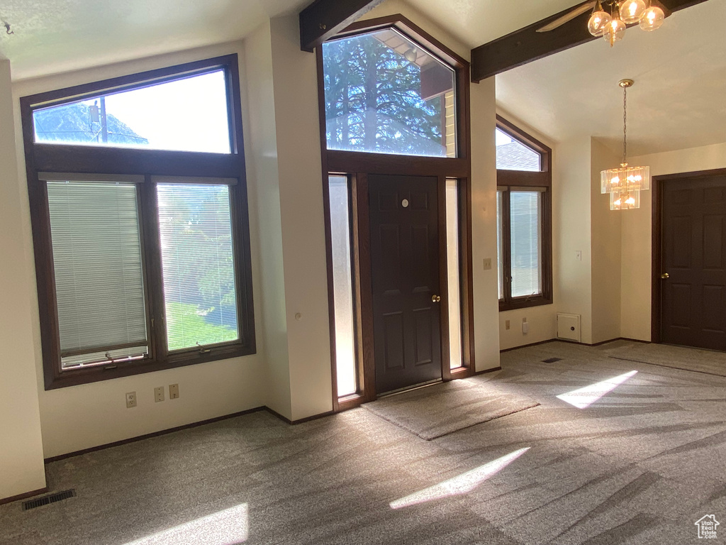 Carpeted foyer featuring high vaulted ceiling, plenty of natural light, and a notable chandelier