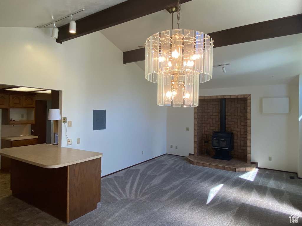 Kitchen featuring a wood stove, a notable chandelier, dark colored carpet, and vaulted ceiling with beams