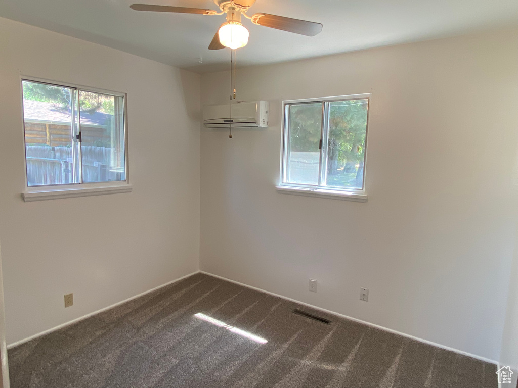 Unfurnished room with a wealth of natural light, a wall unit AC, ceiling fan, and carpet flooring