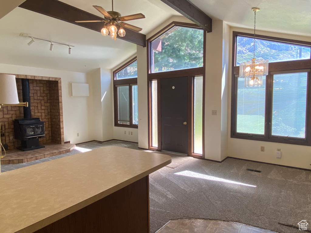 Entryway featuring ceiling fan with notable chandelier, a wood stove, carpet floors, rail lighting, and vaulted ceiling with beams