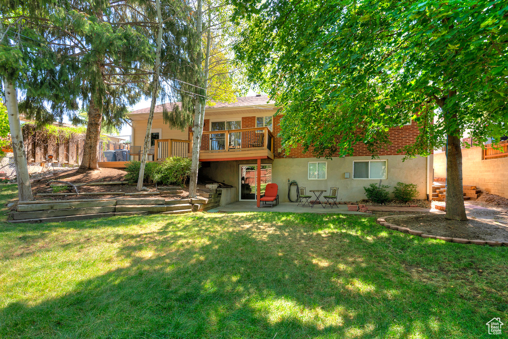 Rear view of property featuring a wooden deck, a lawn, and a patio