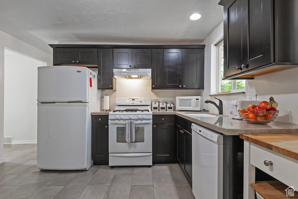 Kitchen featuring white appliances, a textured ceiling, light tile patterned floors, wooden counters, and sink