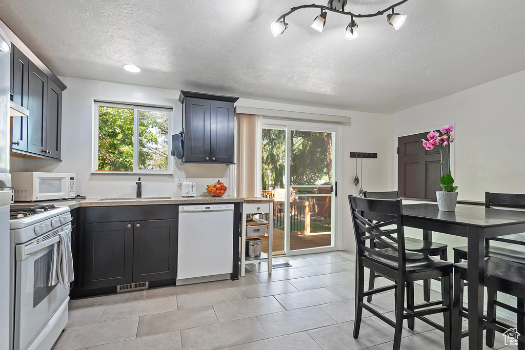 Kitchen with a wealth of natural light, sink, white appliances, and a textured ceiling