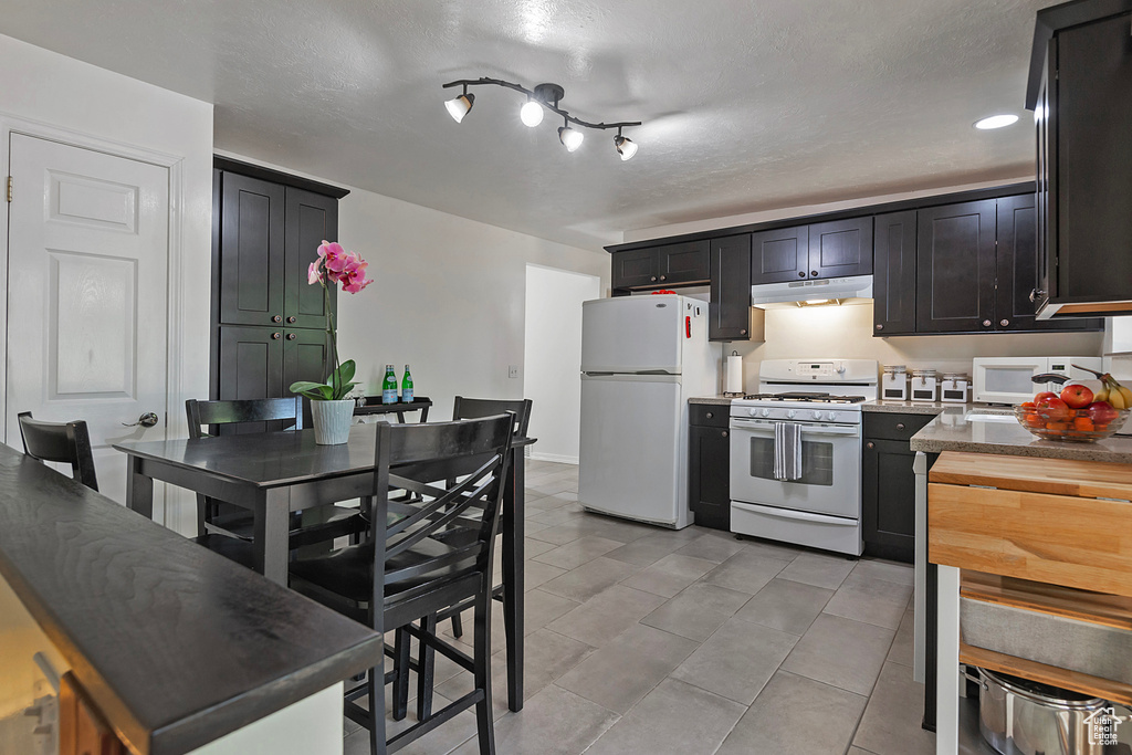 Kitchen featuring a textured ceiling, light tile patterned floors, and white appliances