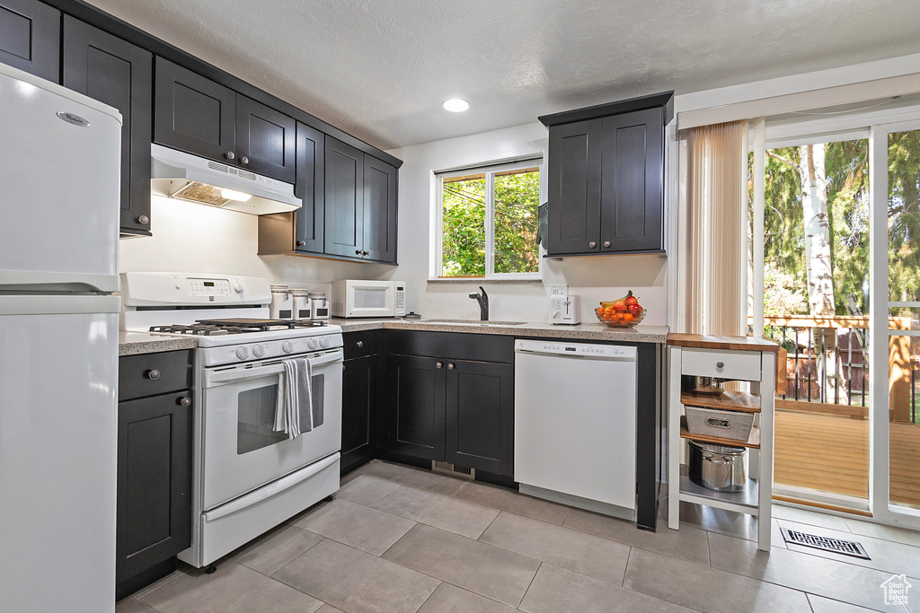 Kitchen with a textured ceiling, sink, white appliances, and light tile patterned flooring