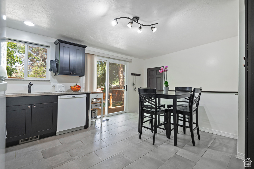 Kitchen featuring light tile patterned floors, white dishwasher, light stone counters, sink, and a textured ceiling