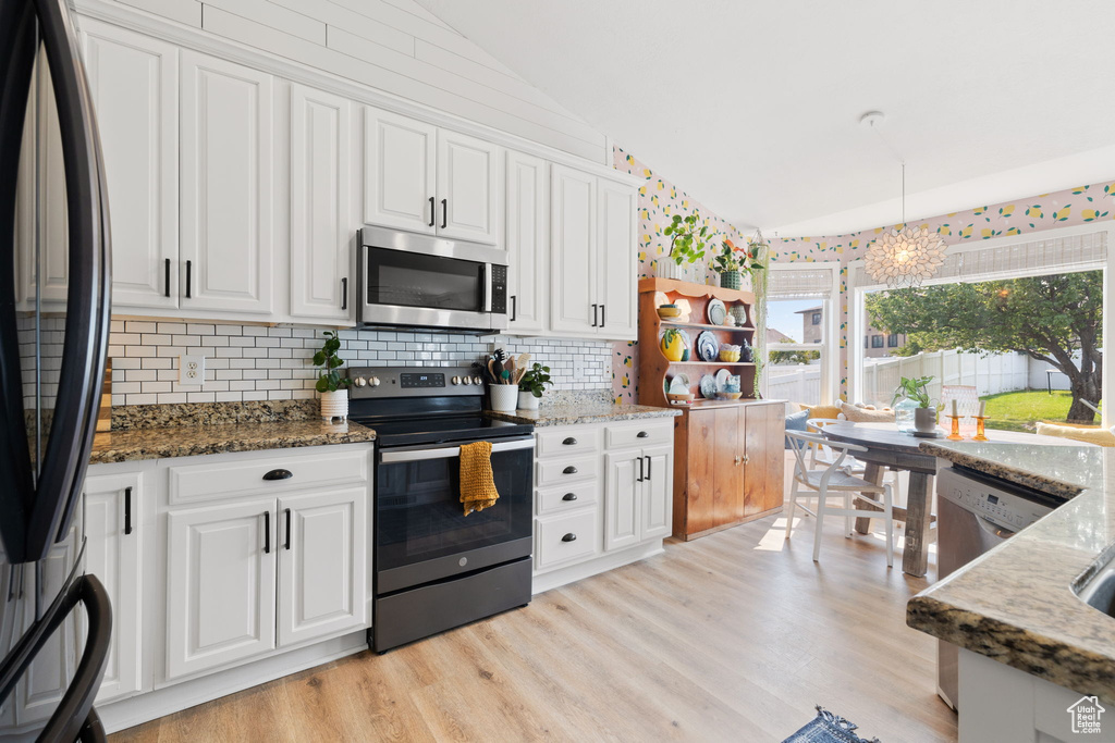 Kitchen with vaulted ceiling, an inviting chandelier, stainless steel appliances, and dark stone counters