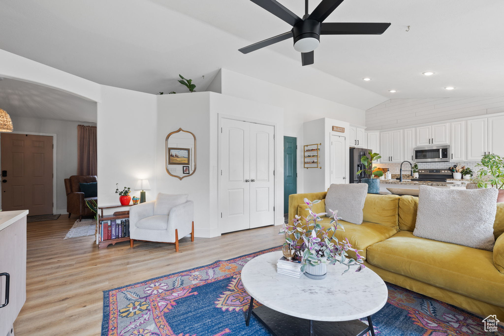 Living room with lofted ceiling, ceiling fan, sink, and light wood-type flooring