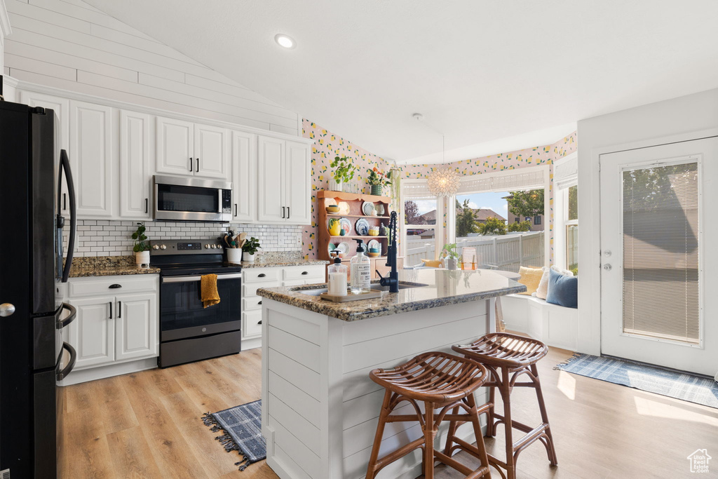 Kitchen featuring stone counters, stainless steel appliances, a breakfast bar, lofted ceiling, and light hardwood / wood-style floors