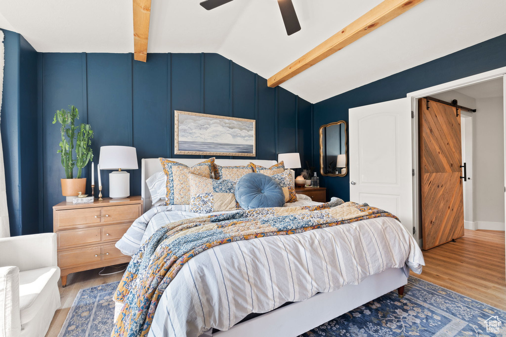 Bedroom with hardwood / wood-style flooring, ceiling fan, a barn door, and vaulted ceiling with beams