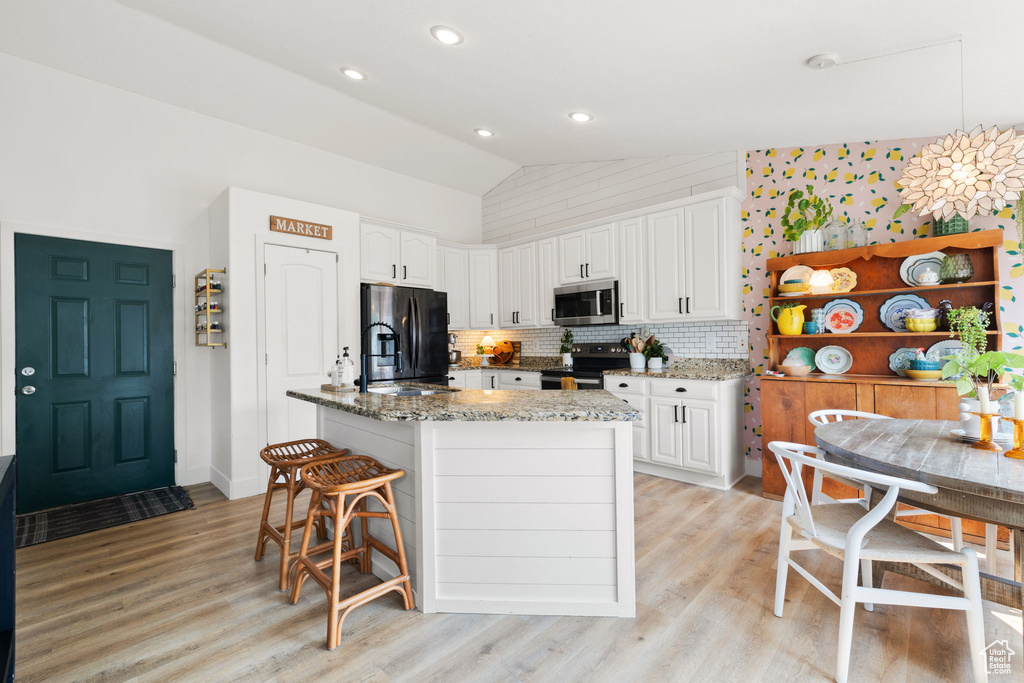 Kitchen with light hardwood / wood-style flooring, stone counters, vaulted ceiling, stainless steel appliances, and white cabinetry