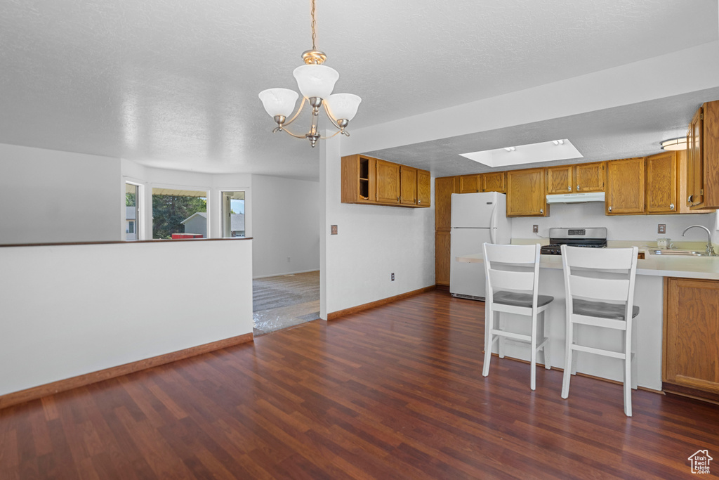 Kitchen featuring an inviting chandelier, stainless steel range oven, white fridge, dark hardwood / wood-style floors, and kitchen peninsula