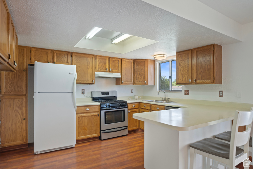 Kitchen featuring white refrigerator, dark hardwood / wood-style flooring, kitchen peninsula, a breakfast bar area, and stainless steel gas range oven