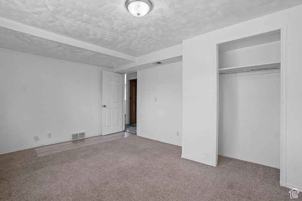 Unfurnished bedroom featuring a closet, light carpet, and a textured ceiling