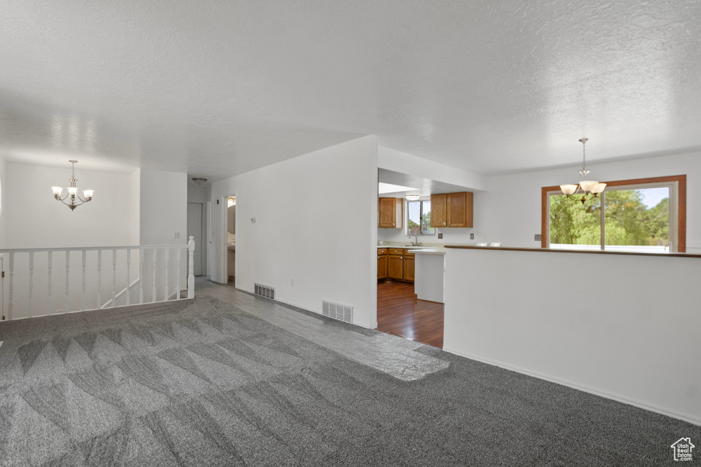 Unfurnished living room with a textured ceiling, an inviting chandelier, sink, and carpet flooring