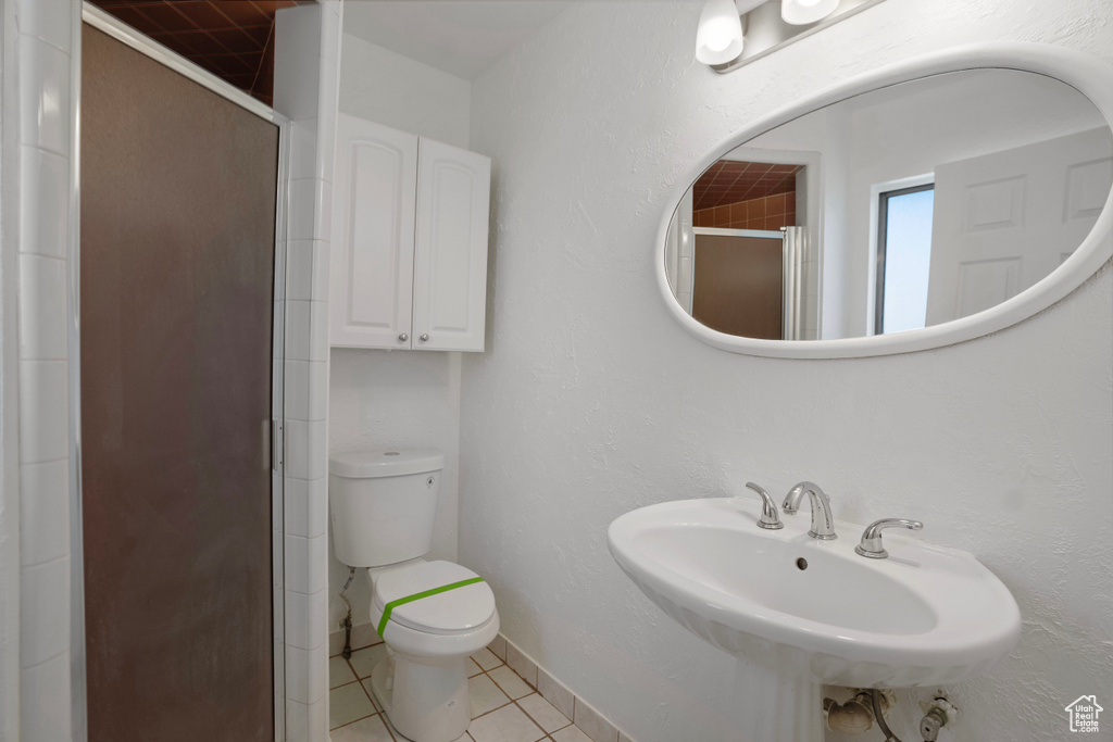 Bathroom featuring a shower with door, toilet, sink, and tile patterned flooring