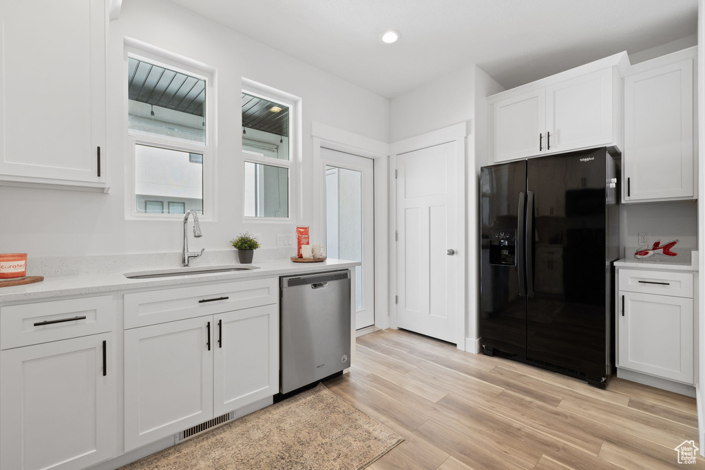 Kitchen with light hardwood / wood-style floors, white cabinetry, sink, black refrigerator with ice dispenser, and stainless steel dishwasher