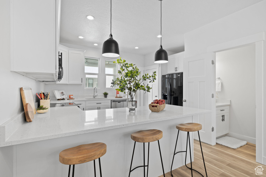 Kitchen featuring black appliances, pendant lighting, white cabinetry, and light hardwood / wood-style flooring