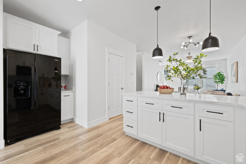 Kitchen with black fridge with ice dispenser, decorative light fixtures, white cabinets, and light hardwood / wood-style floors