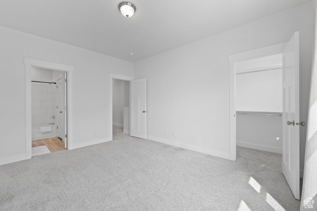 Unfurnished bedroom featuring light colored carpet, connected bathroom, and a closet