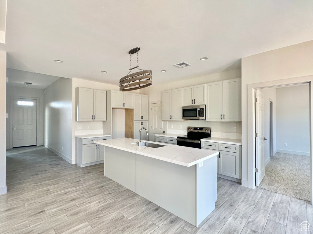 Kitchen with stainless steel appliances, an island with sink, white cabinets, and sink