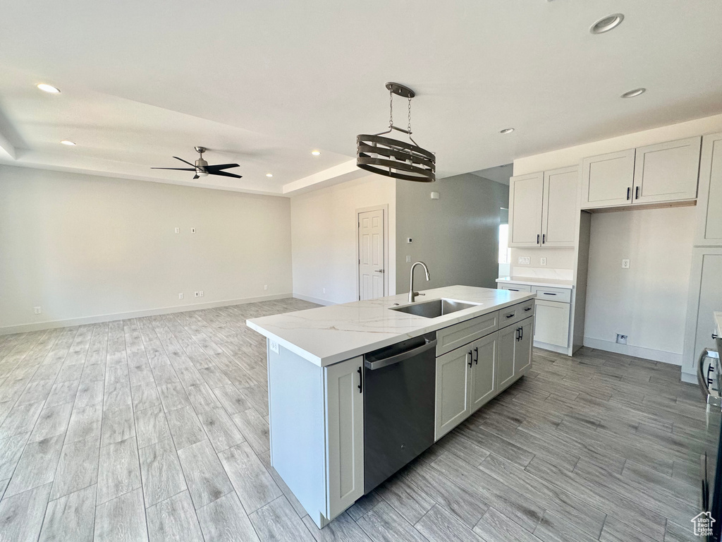 Kitchen with light wood-type flooring, stainless steel dishwasher, white cabinets, sink, and a center island with sink