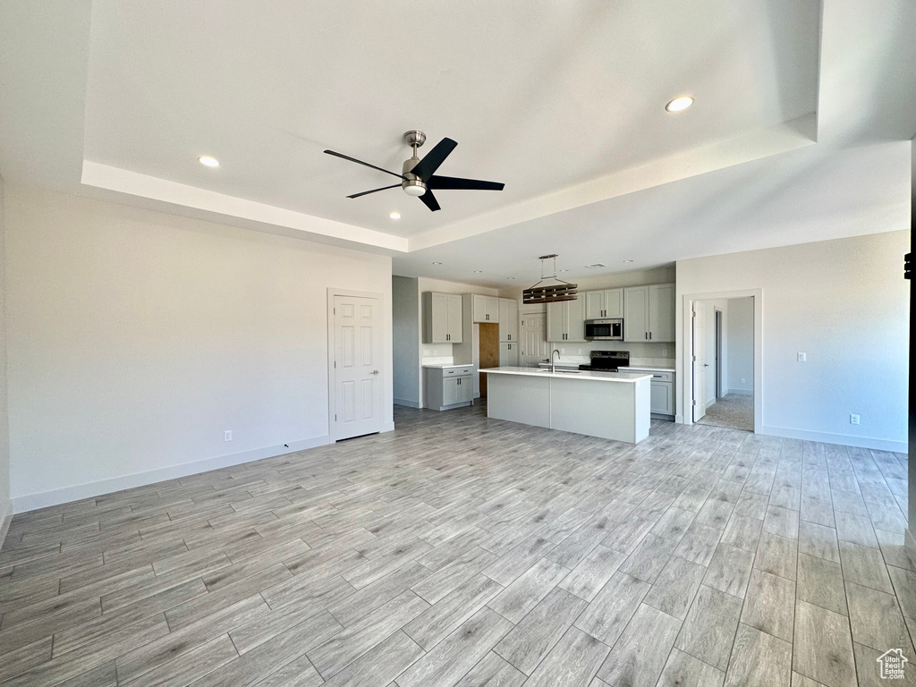 Unfurnished living room with ceiling fan, light wood-type flooring, and a tray ceiling