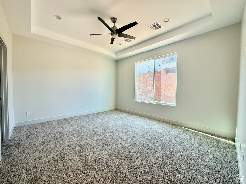 Carpeted empty room featuring ceiling fan and a raised ceiling