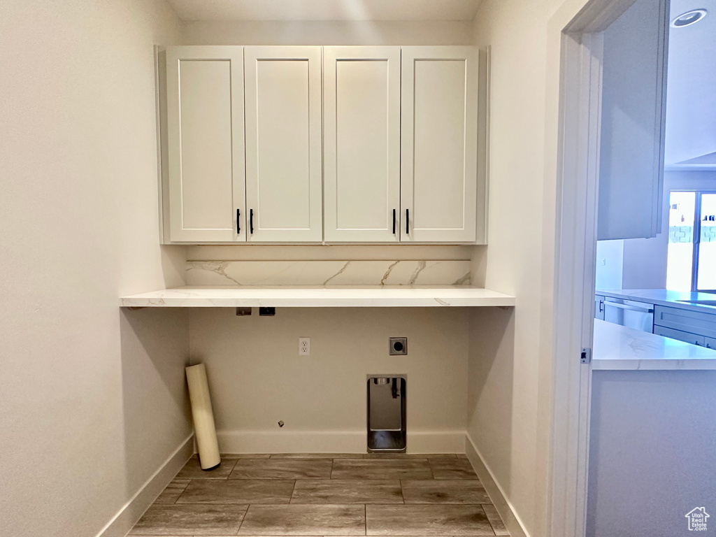 Clothes washing area featuring hardwood / wood-style flooring, hookup for an electric dryer, and cabinets