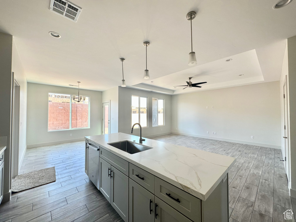 Kitchen featuring light stone counters, a kitchen island with sink, sink, light hardwood / wood-style floors, and decorative light fixtures