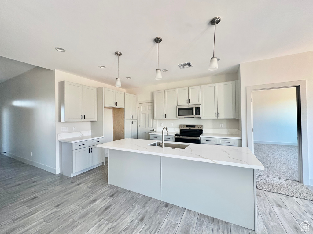 Kitchen with light hardwood / wood-style floors, a center island with sink, decorative light fixtures, sink, and appliances with stainless steel finishes