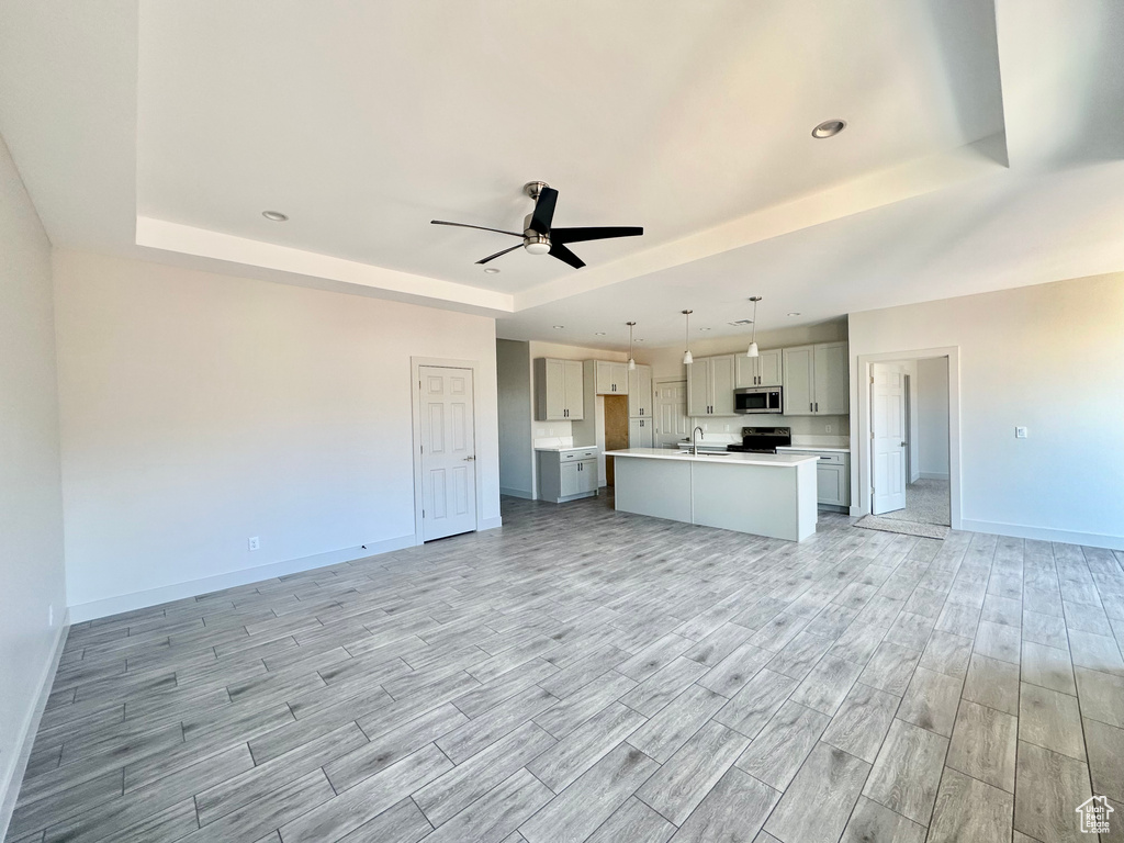 Unfurnished living room featuring ceiling fan, light wood-type flooring, a tray ceiling, and sink