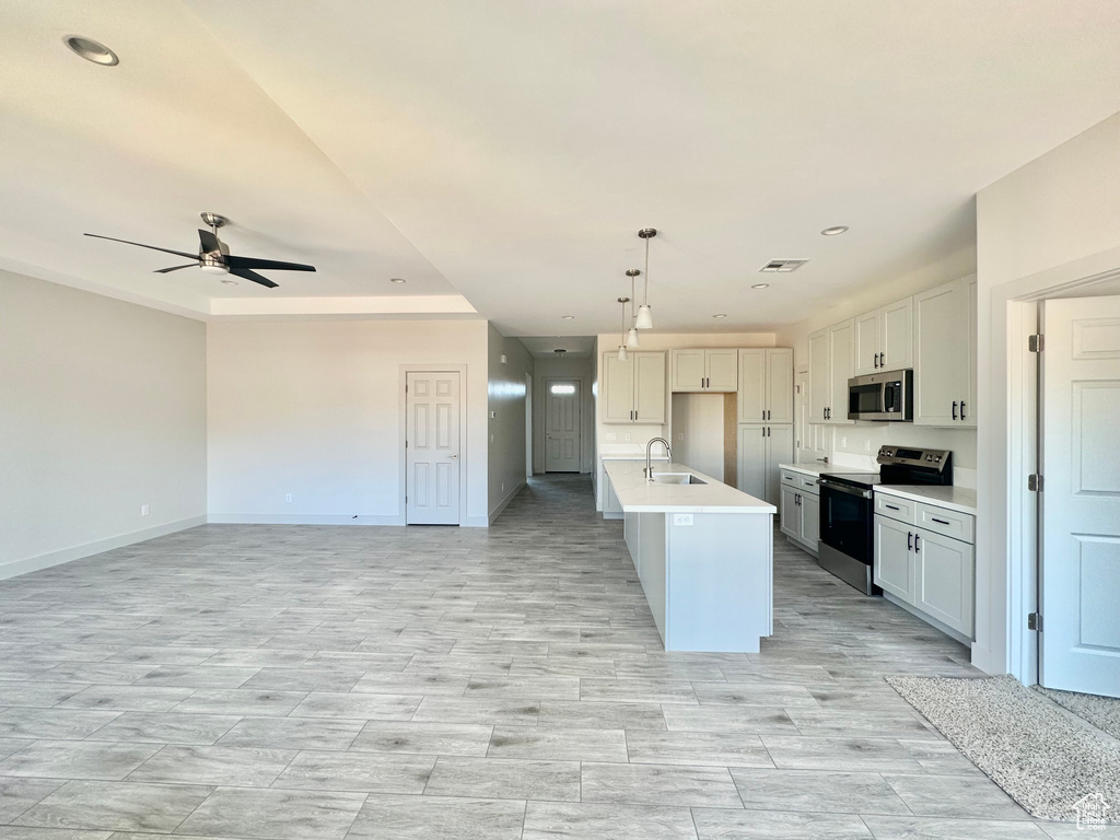 Kitchen featuring an island with sink, sink, decorative light fixtures, white cabinetry, and stainless steel appliances