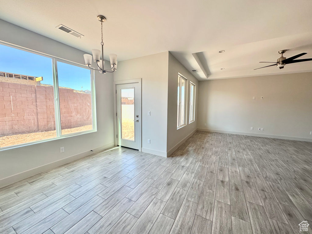 Unfurnished room with ceiling fan with notable chandelier, plenty of natural light, and light hardwood / wood-style floors