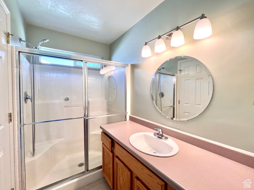 Bathroom featuring a shower with door, a textured ceiling, and vanity