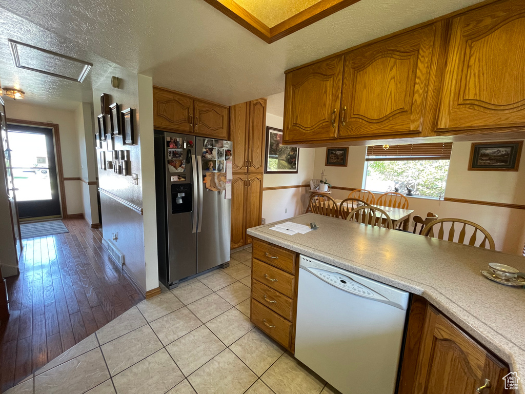 Kitchen featuring light wood-type flooring, stainless steel fridge, white dishwasher, and a textured ceiling