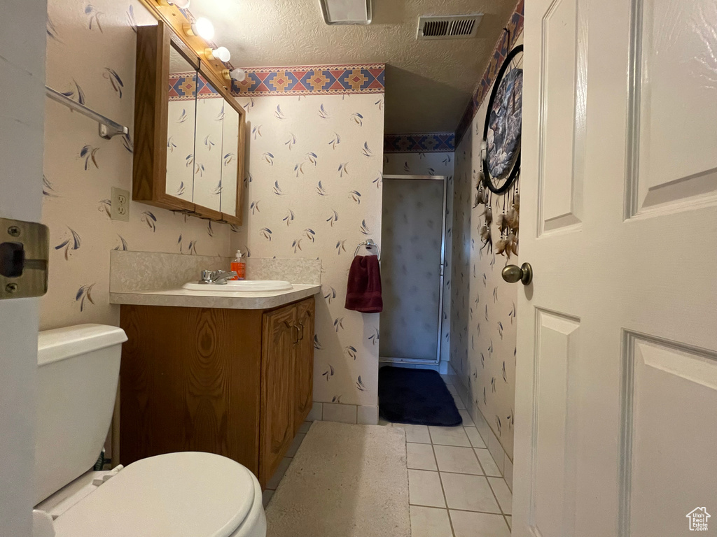 Bathroom with a textured ceiling, tile patterned floors, walk in shower, toilet, and vanity