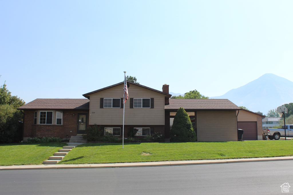 Split level home featuring a mountain view, a garage, and a front lawn