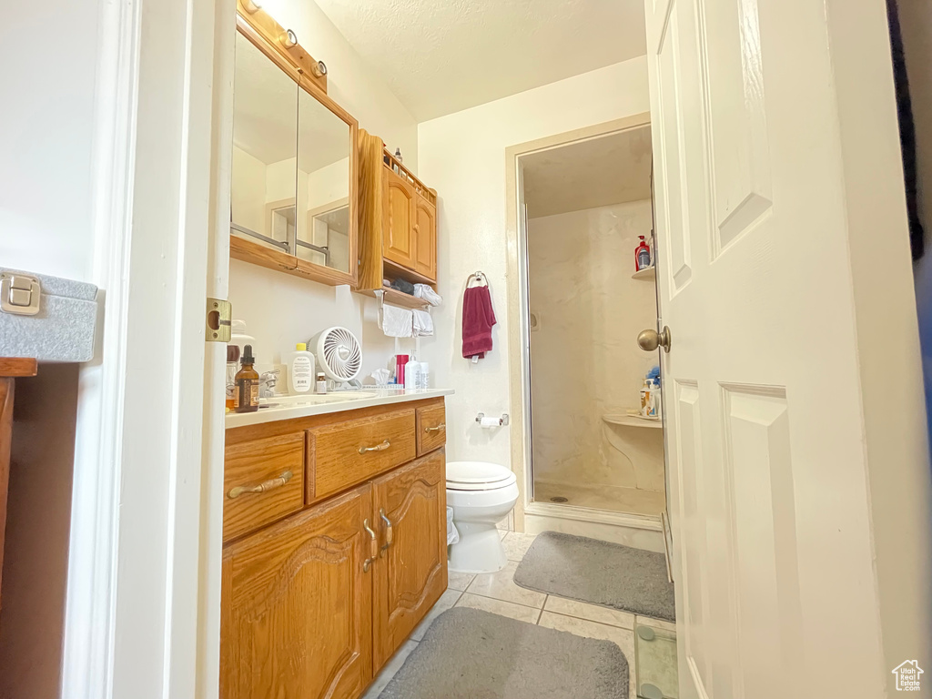 Bathroom featuring tile patterned floors, toilet, a shower with door, and vanity