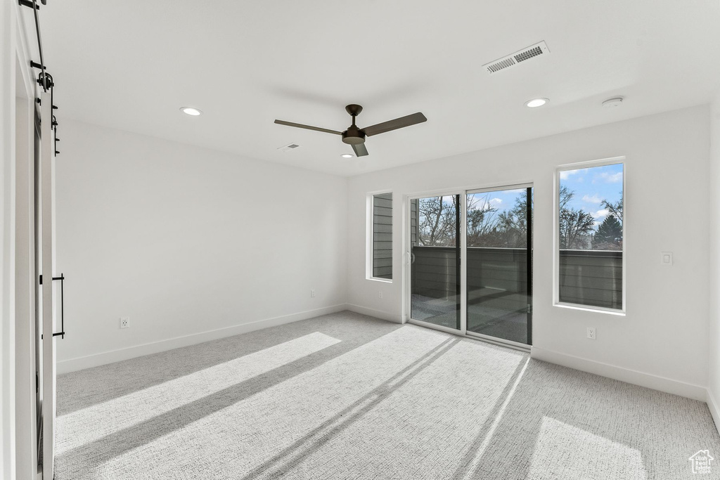 Unfurnished room featuring light colored carpet, ceiling fan, and a barn door