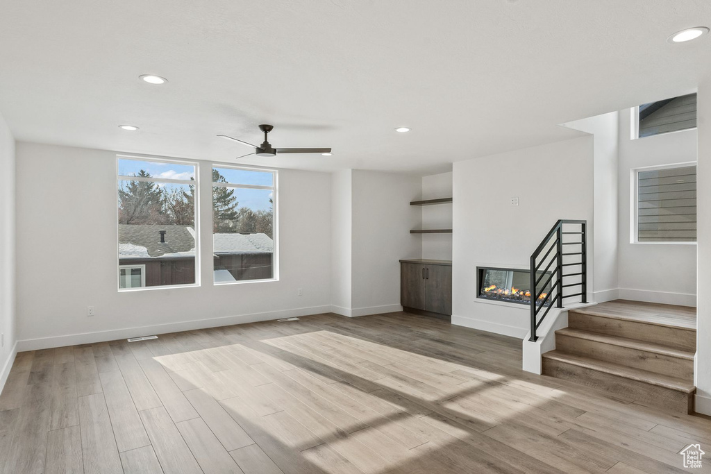 Unfurnished living room featuring ceiling fan, a multi sided fireplace, and light hardwood / wood-style flooring