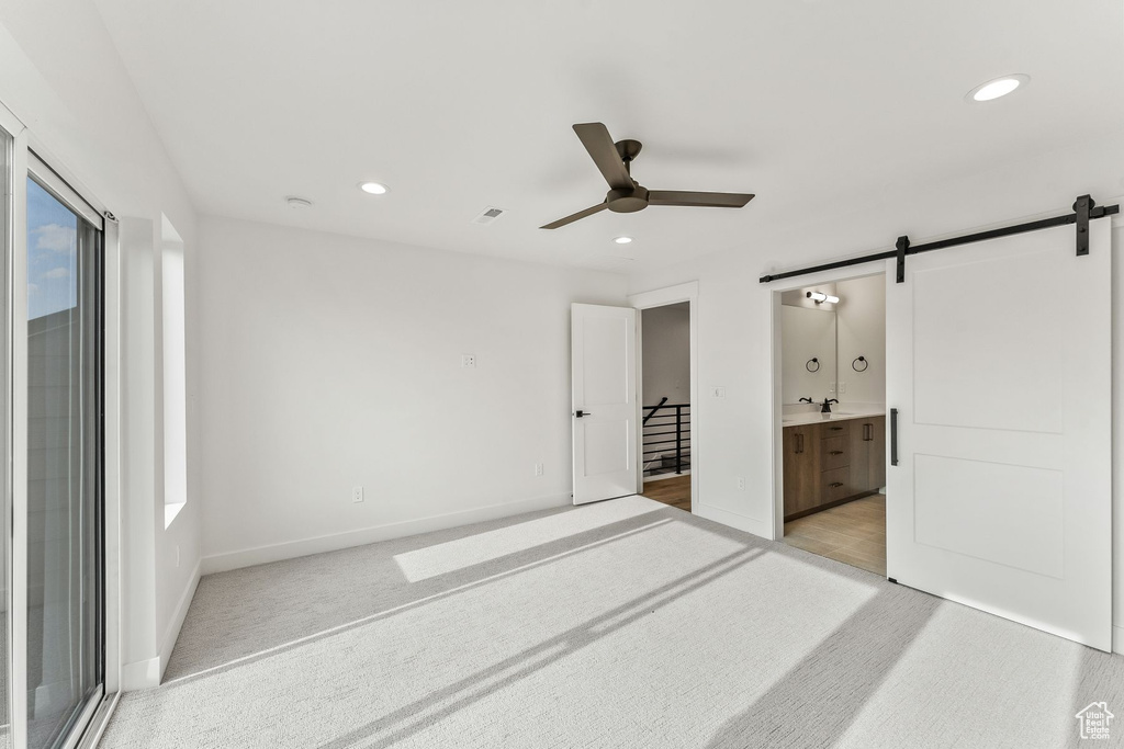 Carpeted bedroom with a barn door, ensuite bath, and ceiling fan