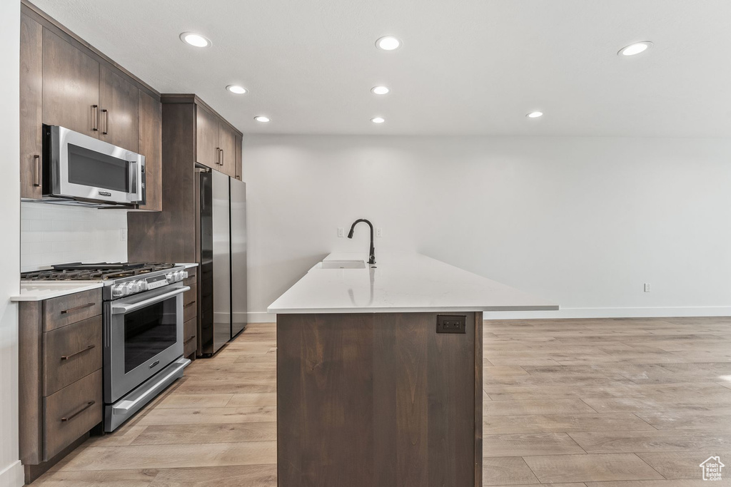 Kitchen with light wood-type flooring, a center island, stainless steel appliances, and sink