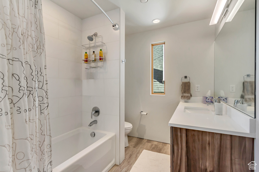 Full bathroom with wood-type flooring, toilet, shower / tub combo with curtain, and vanity